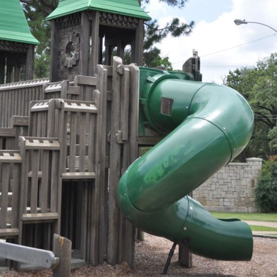 A green slide attached to a wooden playground structure with a peaked roof.