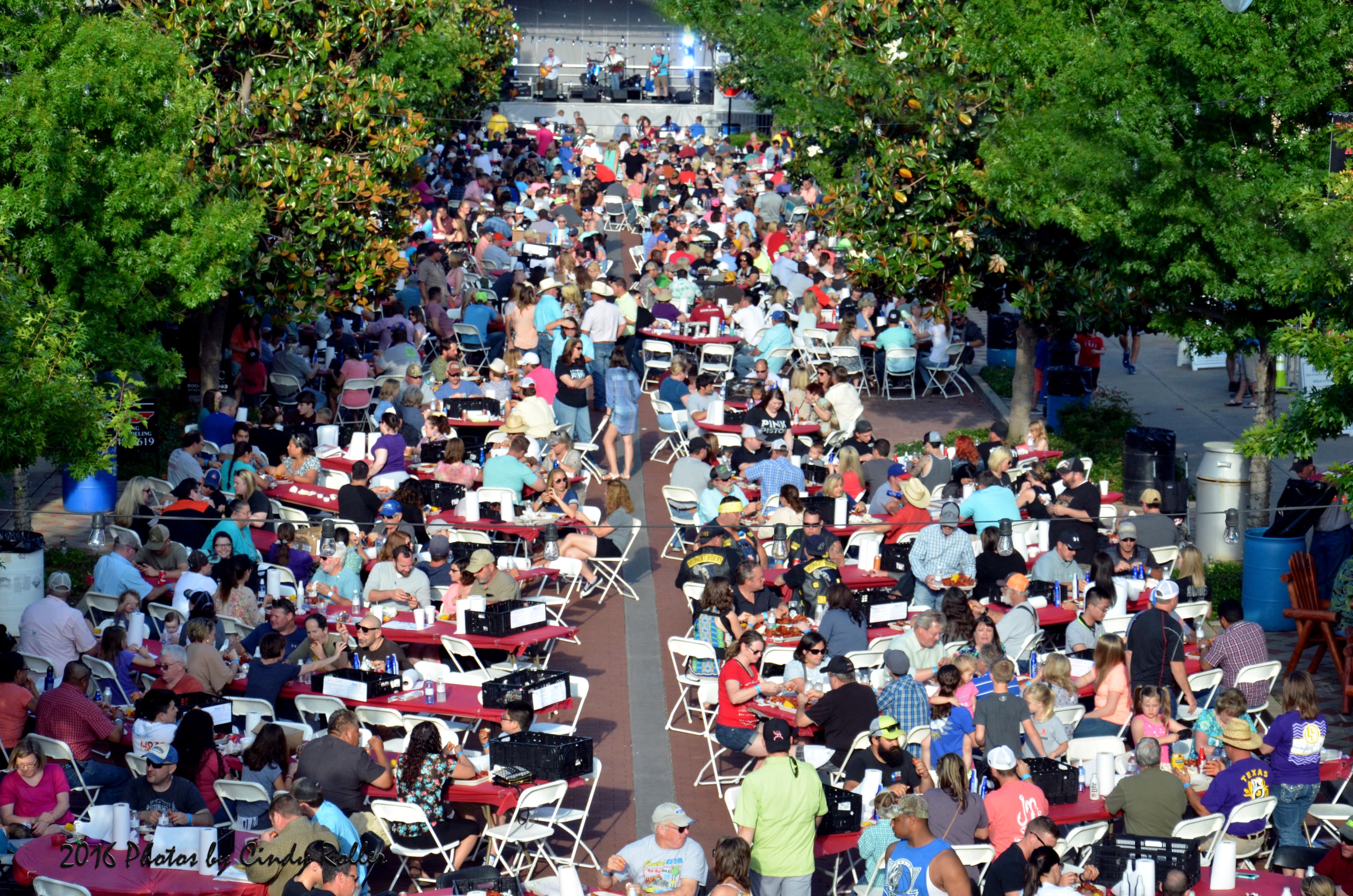 A large crowd of people sits at tables in a busy outdoor dining area surrounded by trees.