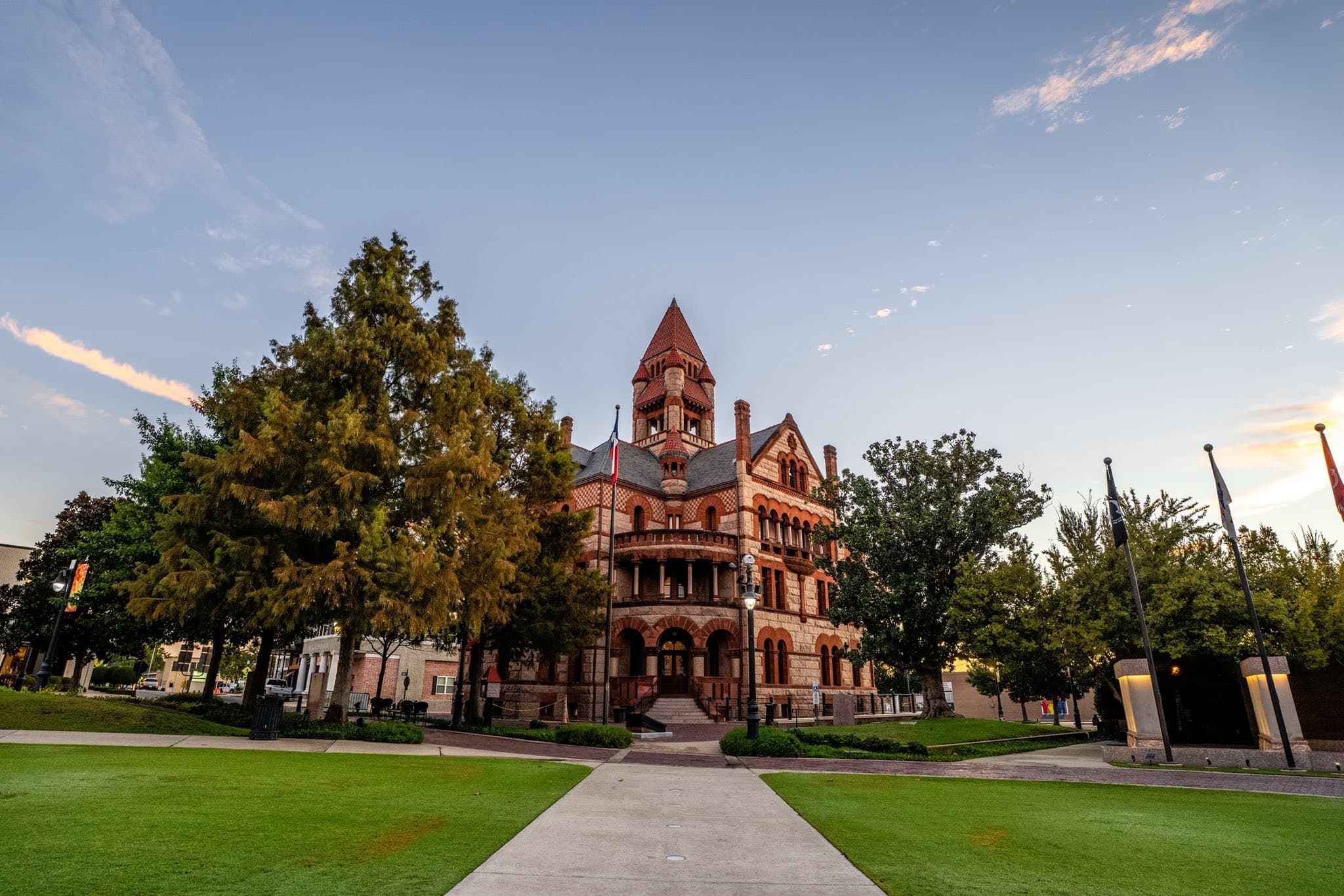 Historic building with a tall clock tower surrounded by trees and green grass.