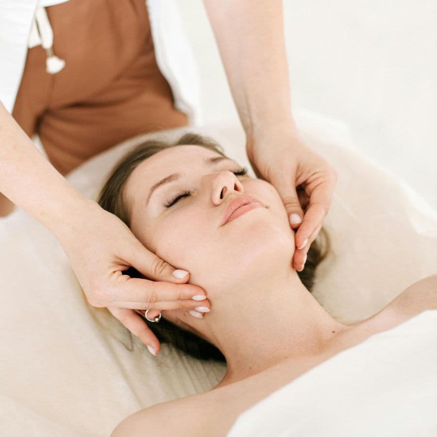 A woman receives a facial massage with her eyes closed, looking relaxed.