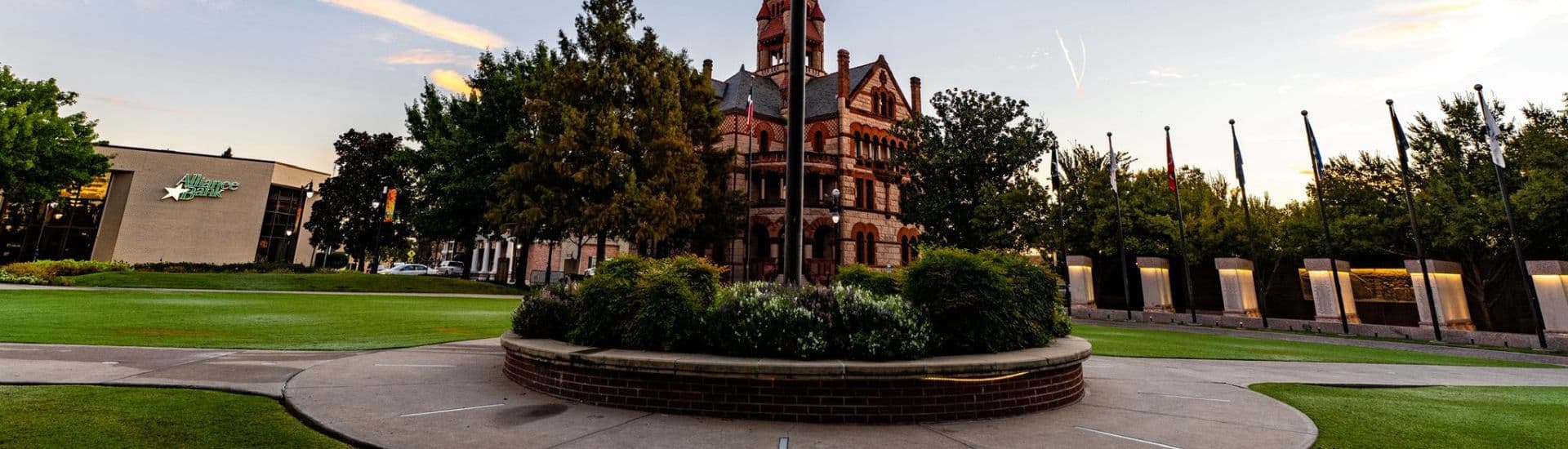 Historic building surrounded by landscaped lawn and trees at sunset.