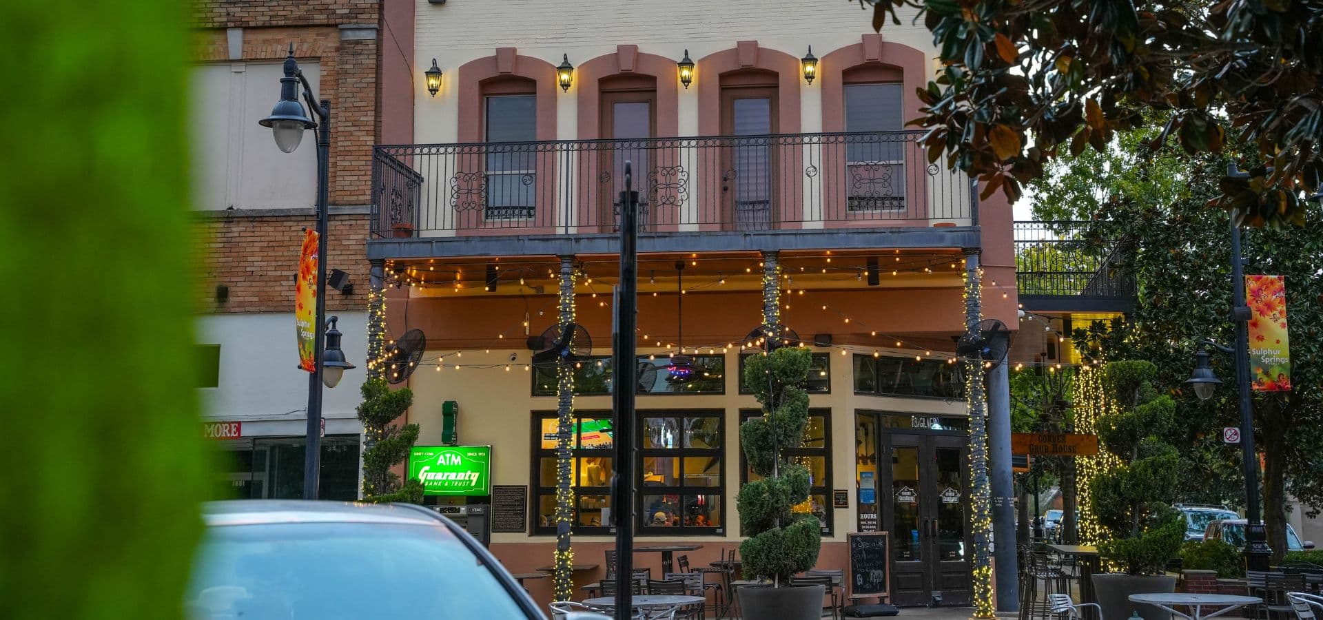 A charming restaurant building adorned with lights and greenery, featuring a balcony and outdoor seating.