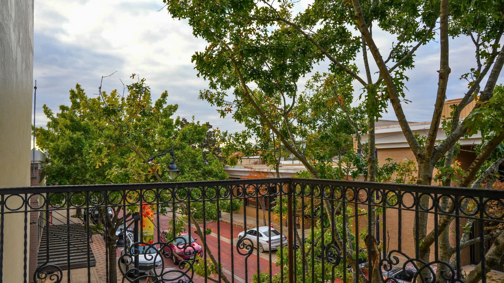 A balcony view featuring lush trees and parked cars along a colorful street.