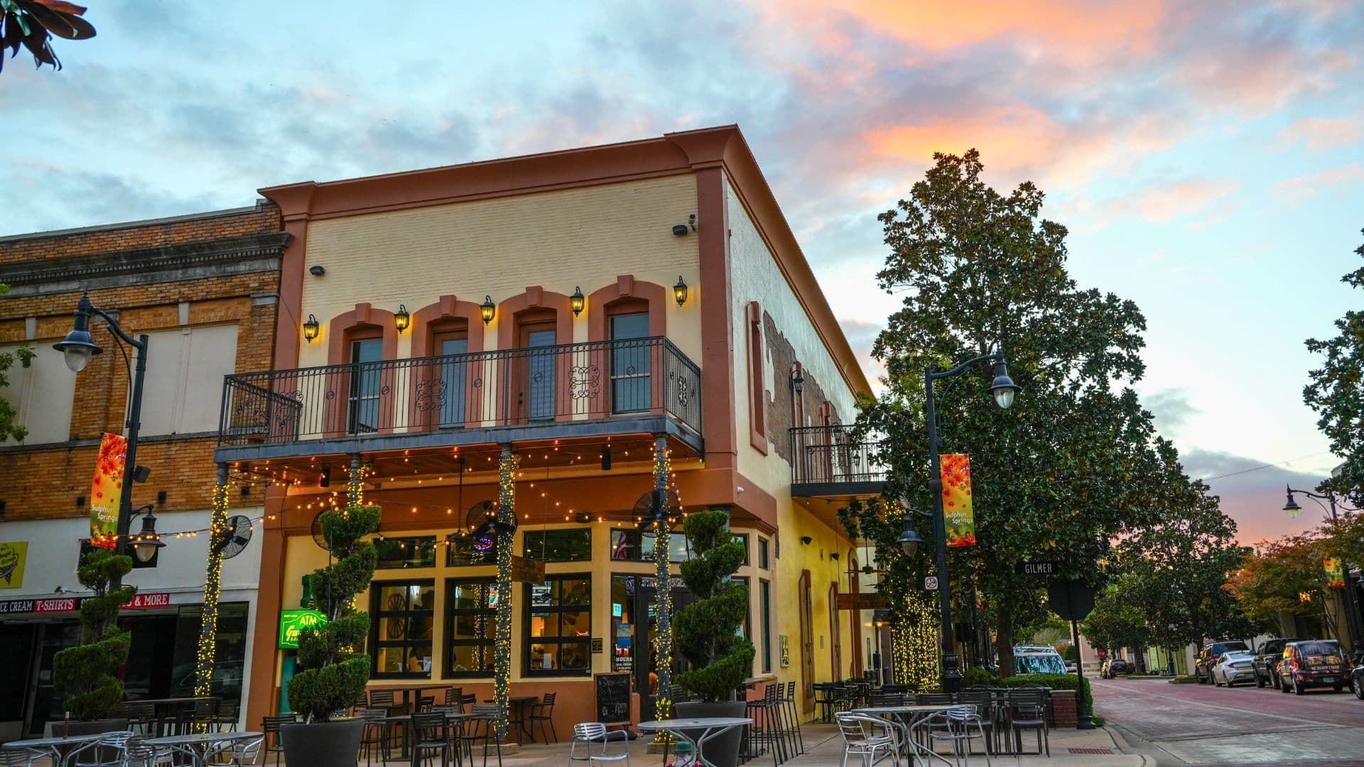 A charming multi-story restaurant with outdoor seating, surrounded by greenery and decorative lights at sunset.