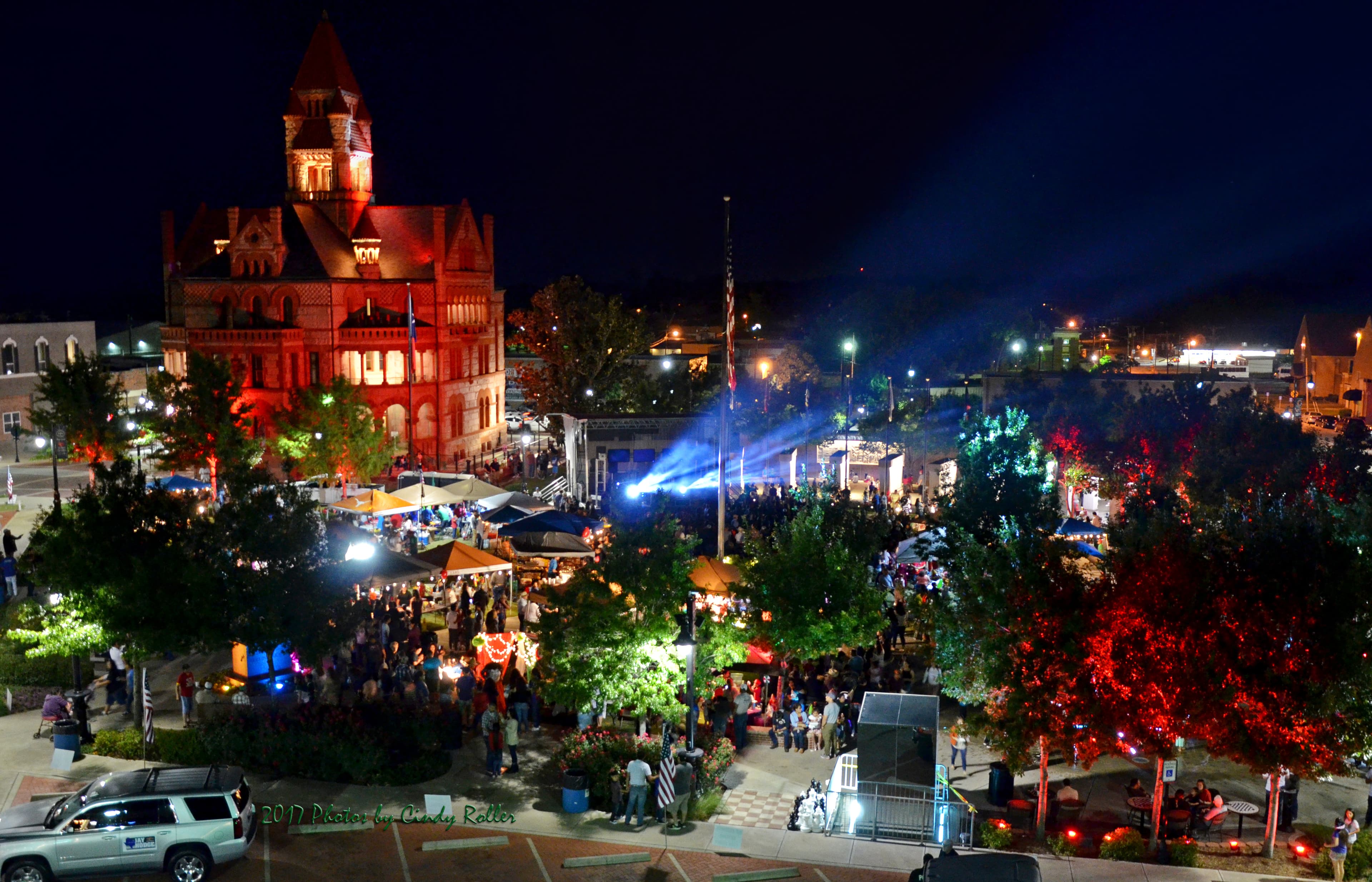 A vibrant night scene of a bustling outdoor festival with tents, lights, and a historic building in the background.